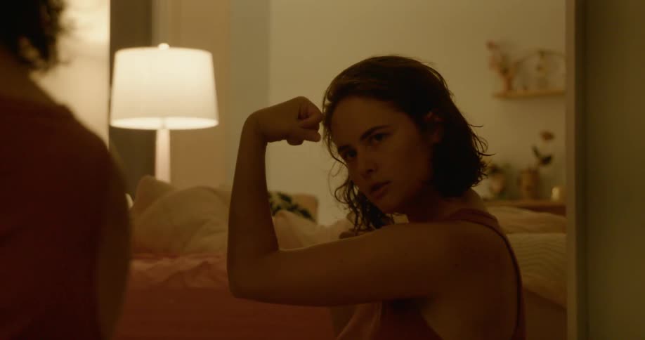 A teenager looking in a mirror blows a kiss and flexes her muscles