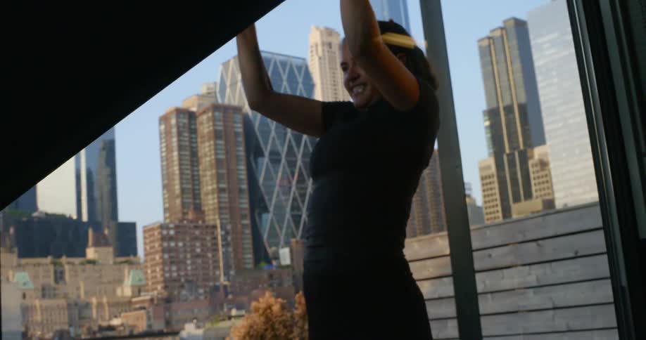 A young woman does pullups outdoors as skyscrapers loom in the sky behind her