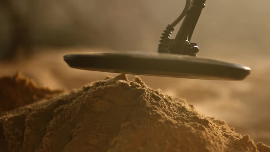 Metal detector hovers over mound of sand