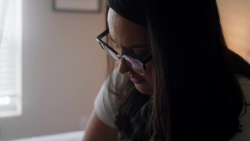 Woman sitting on bed looks down as she works