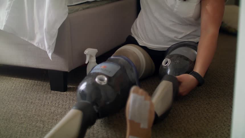 A female caucasian sitting on the floor adjusting her prosthetic legs