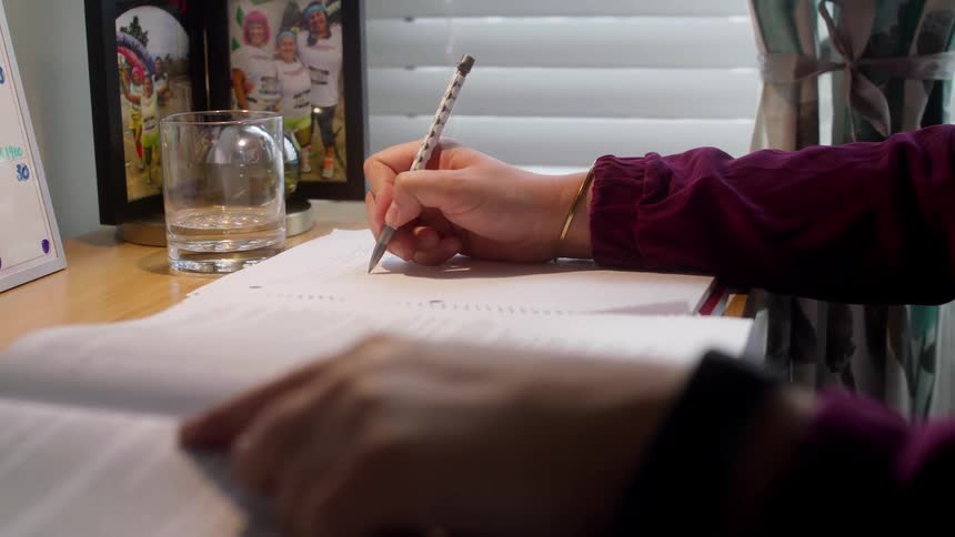A woman sits at a desk writing on a piece of paper