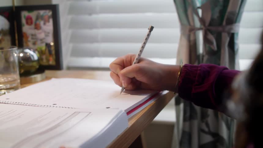 A young woman does her homework at a desk next to a window during the day