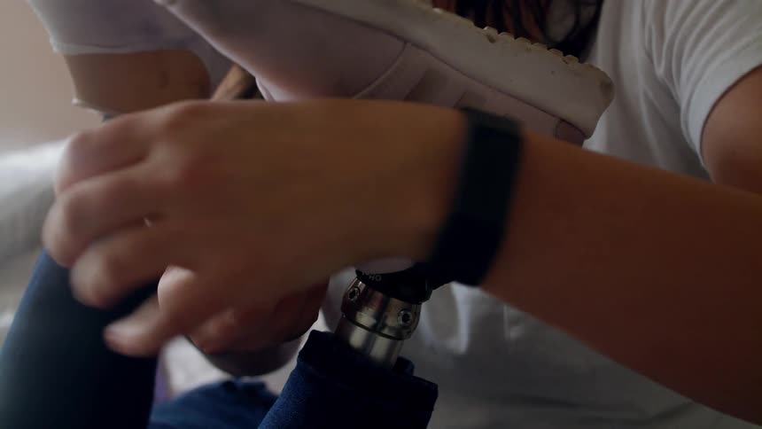 Woman tying sneakers on the feet of prosthetic legs while sitting in bed at home