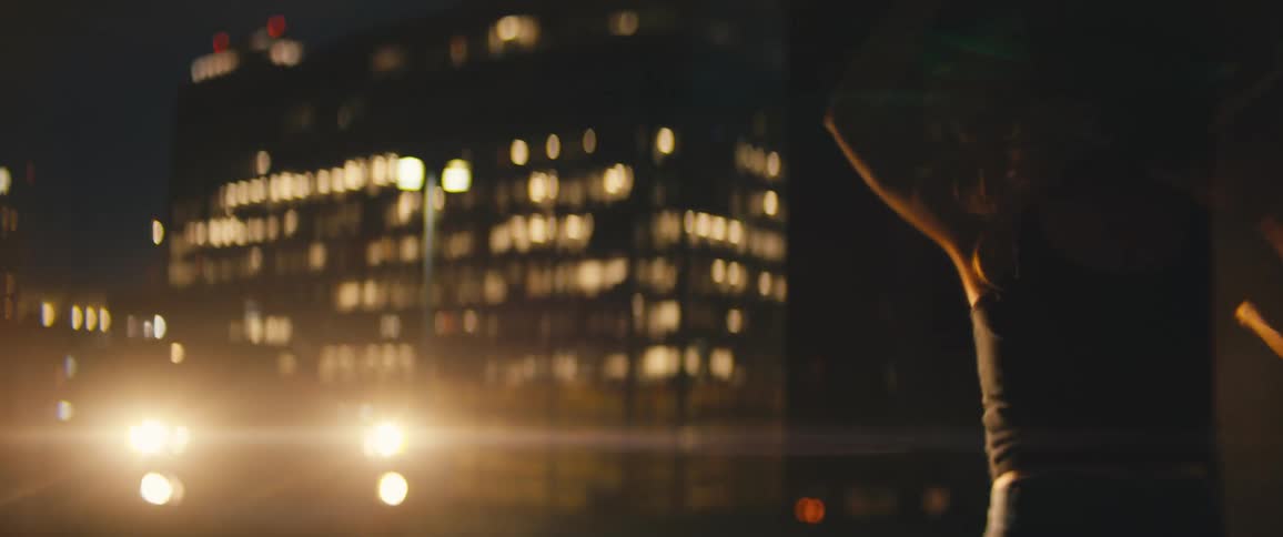 Silhouette of young woman dancing in front of the headlights of a car in the city at night