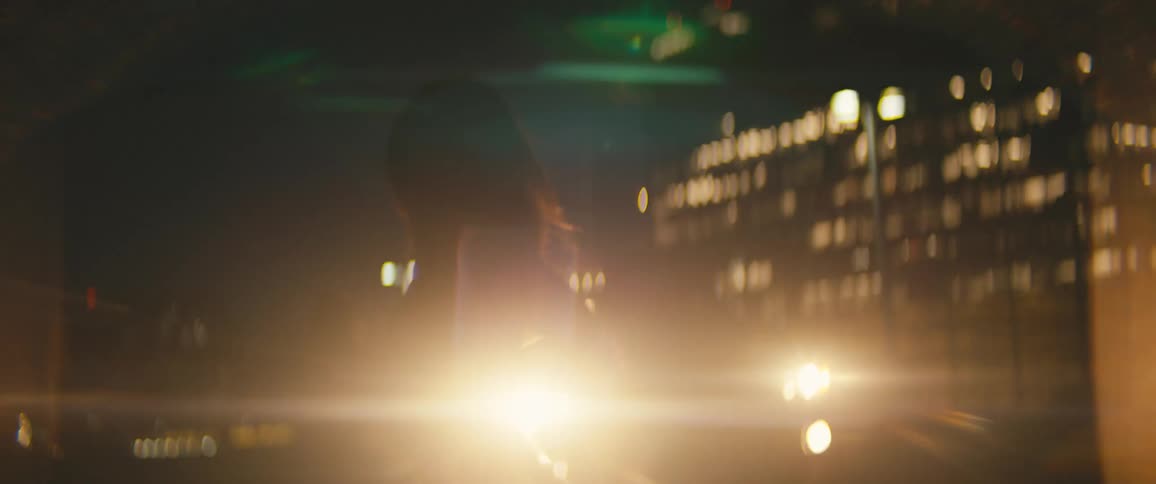 A woman dances outside at night in front of the headlights of a parked vehicle