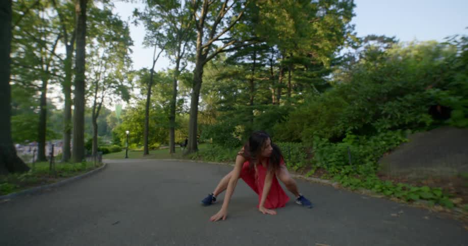 A woman in a dress dances in a strange manner while outdoors