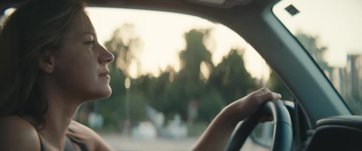 The wind blows through a young womans hair as she drives a vehicle down a city street during the day