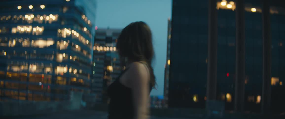 A young woman spins around and dances on a rooftop with the skyline behind her