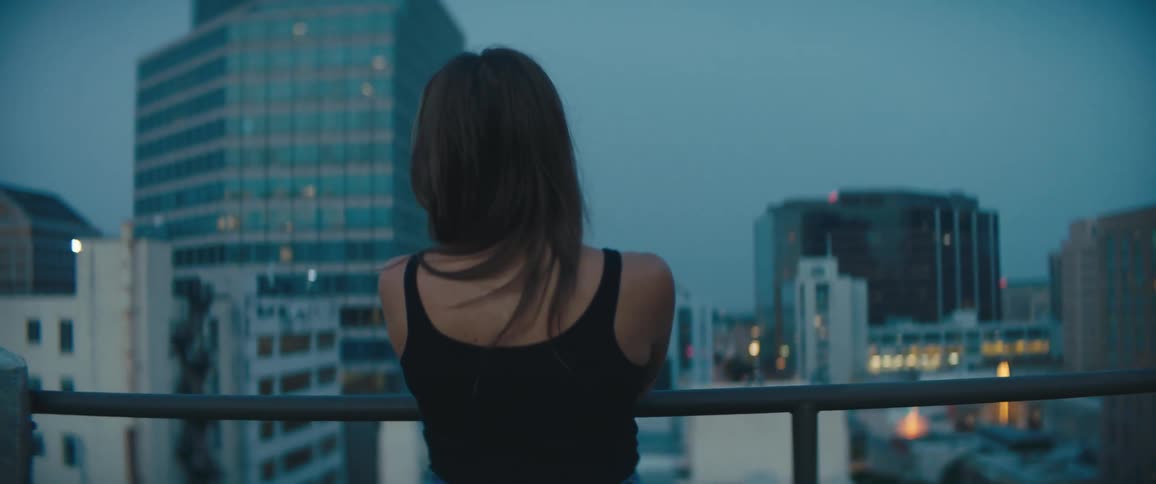 A woman stands leisurely on a rooftop in a metropolis at night