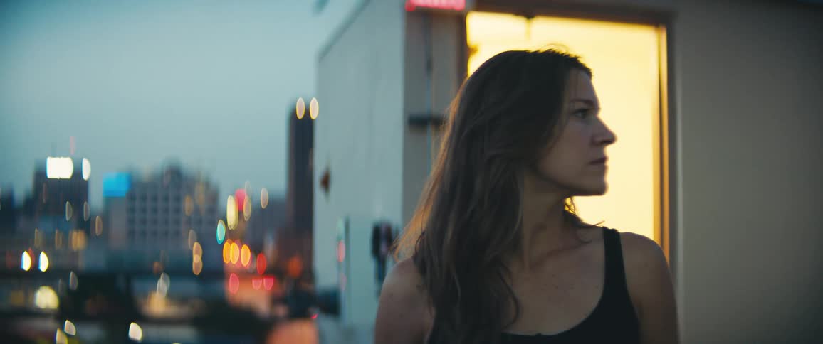 Woman with brown hair looks to the left and turns her gaze to the camera at dusk