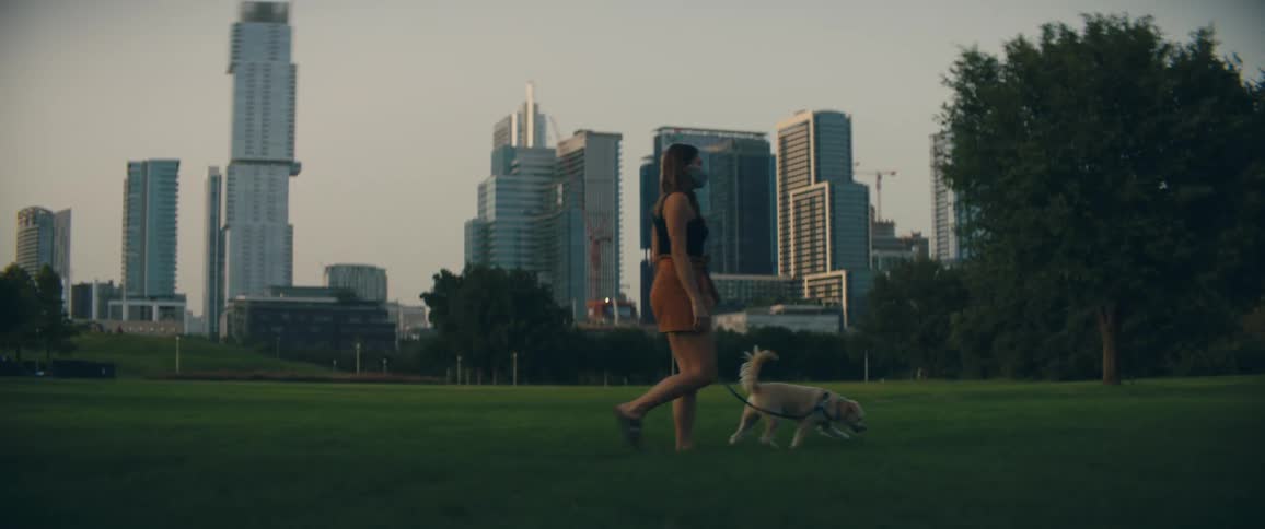 A woman walks her small dog across the lawn in a park near downtown