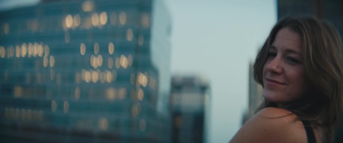 A woman stands leisurely on a balcony in a metropolis in the evening