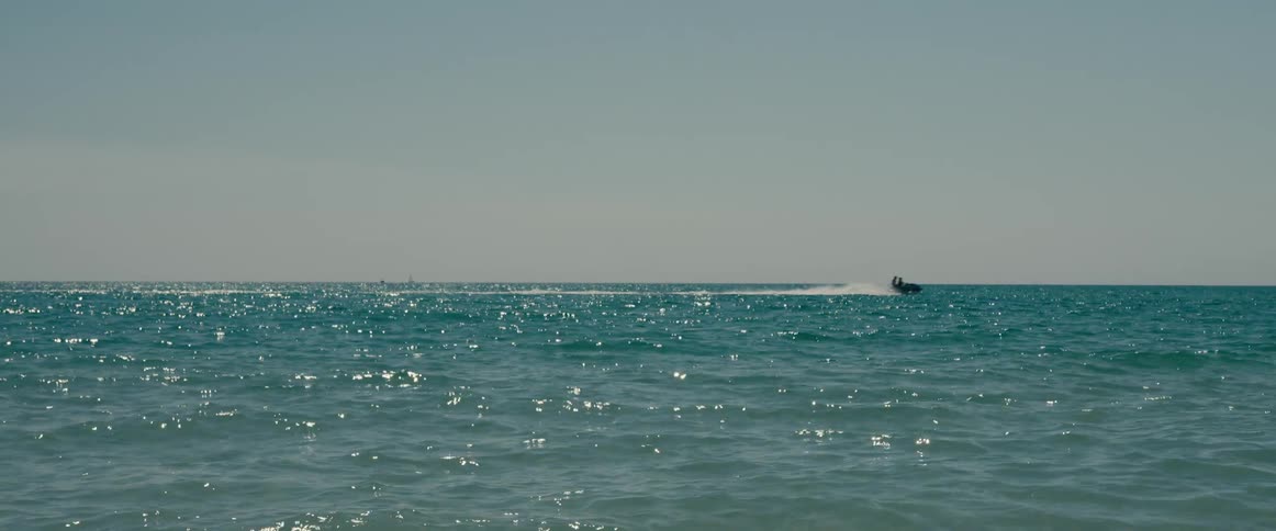 A pair of people riding on a jet ski speed across the ocean on a sunny day