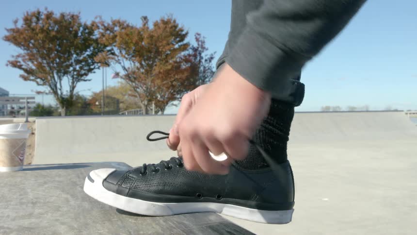 Someone ties their shoes as another skates in a park