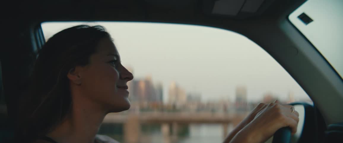 Side view of a woman driving over a bridge with city skyline in the background