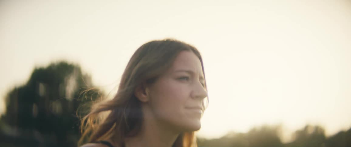 A female caucasian walking near a grass and trees