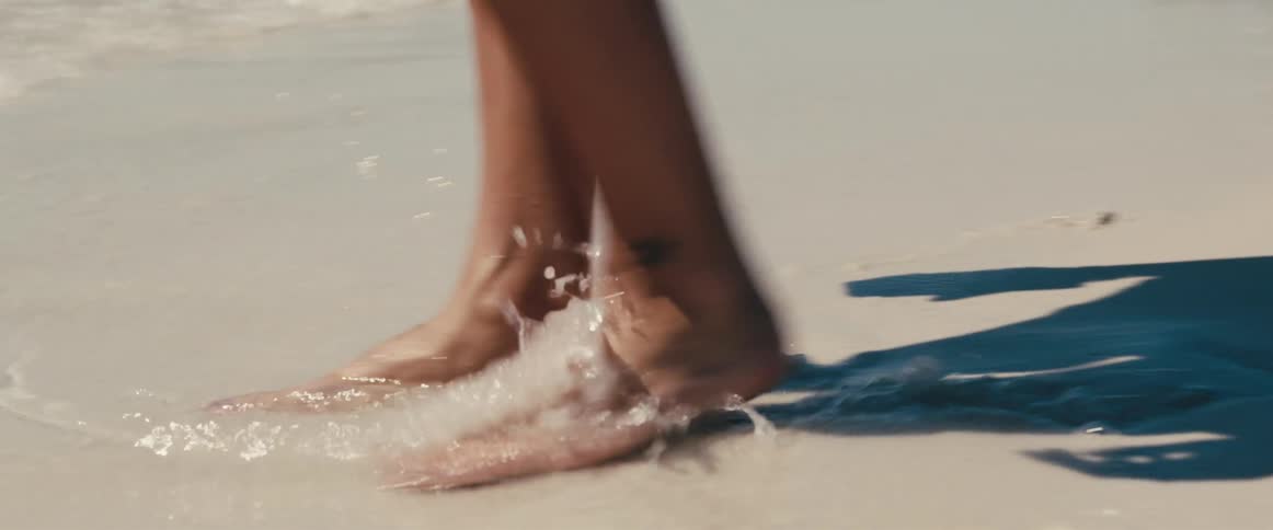 A barefoot woman draws in wet sand with her toes on a beach