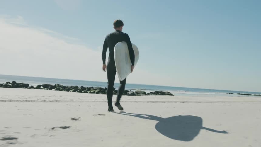A man is walking towards the water carrying a surfboard