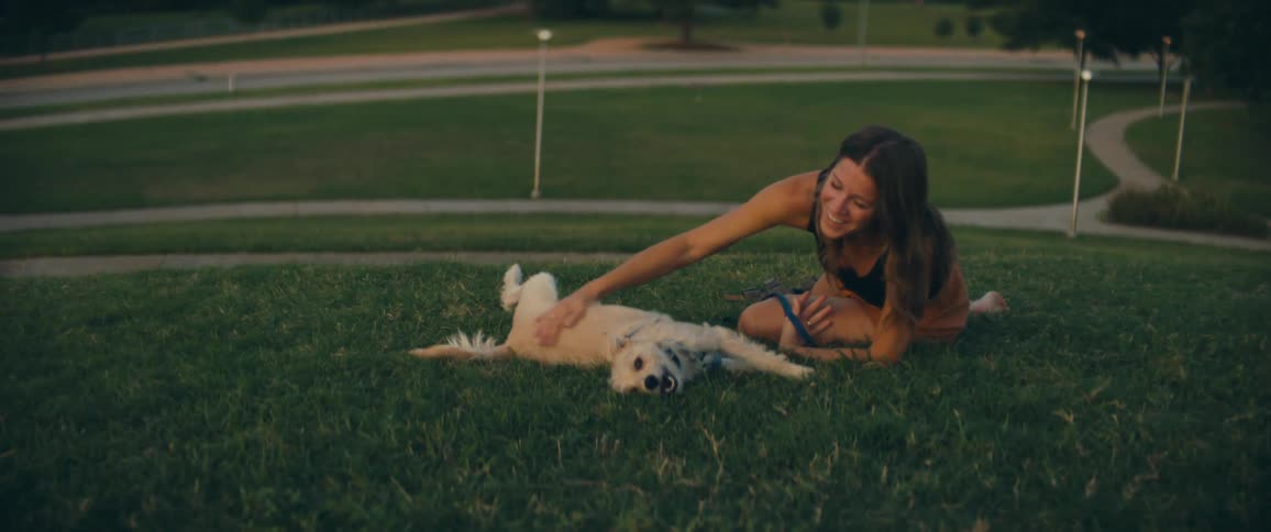 A caucasian female sitting on grass petting a dog