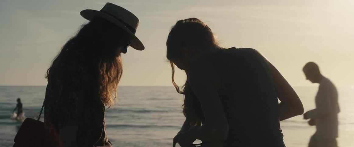 A trio of young women stand together on a beach at sunset and gaze at the palm of one of the womens hand