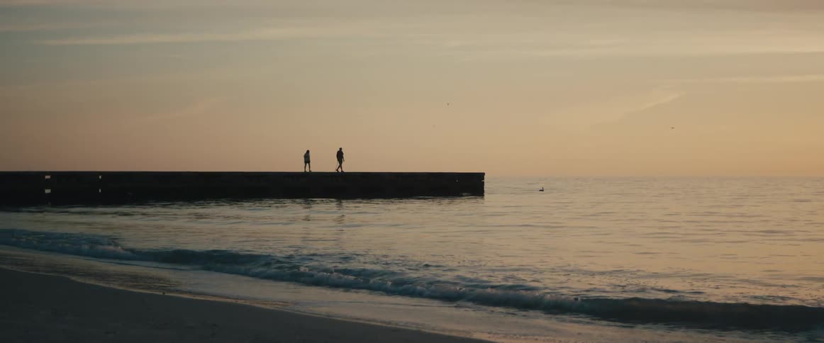 Couple walking over a pier in the calm ocean waters at sunset