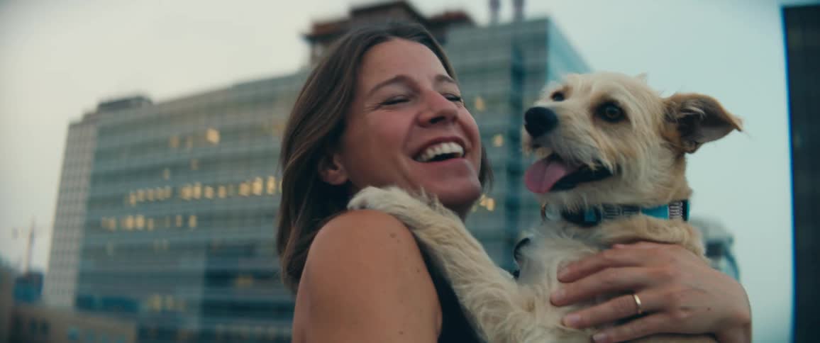A woman holds her dog standing outside in a large city