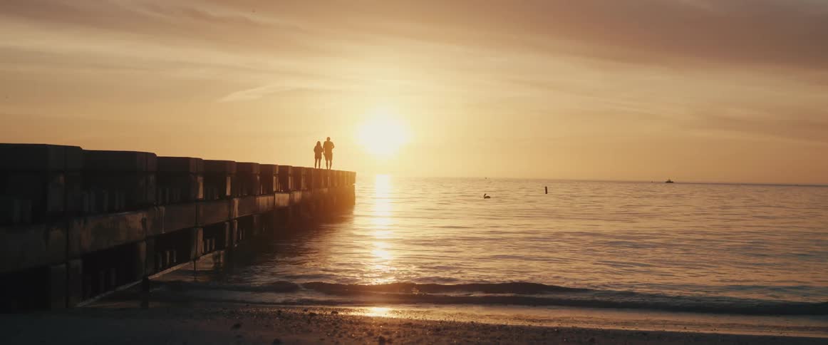 Two people standing on a pier as a bird swims by