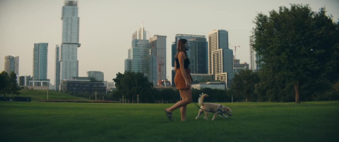 A female caucasian walking her dog on grass near buildings