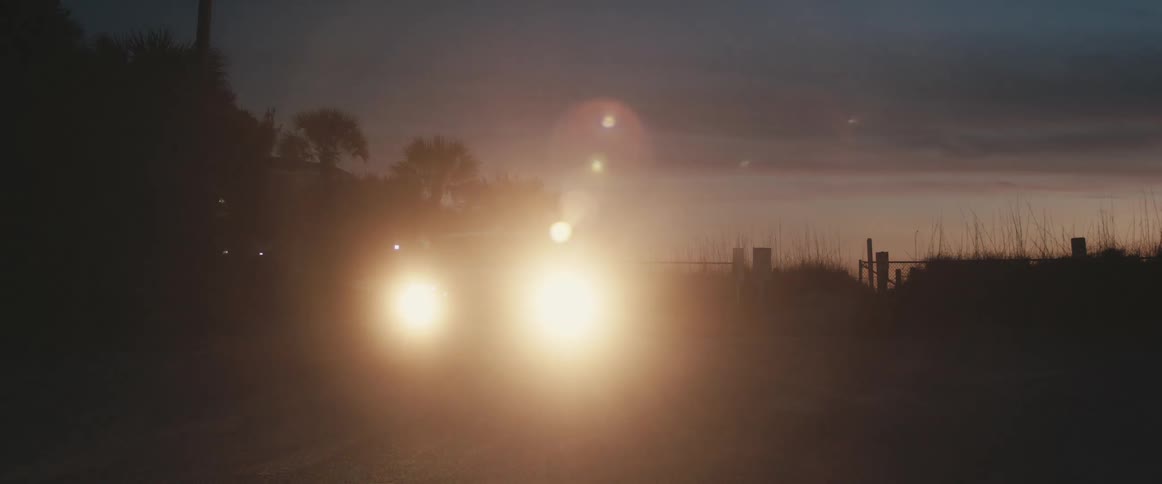 A vehicle performs a uturn on a road outside of field at sunset