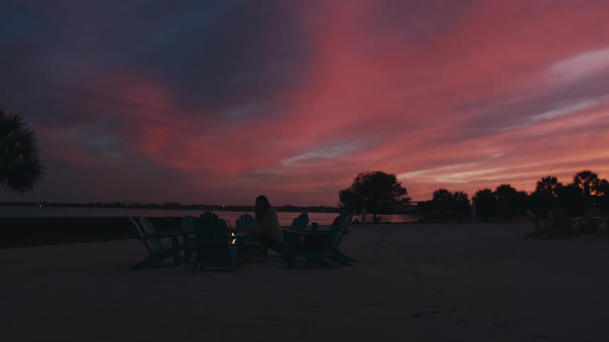 A woman sitting by a fire on the beach