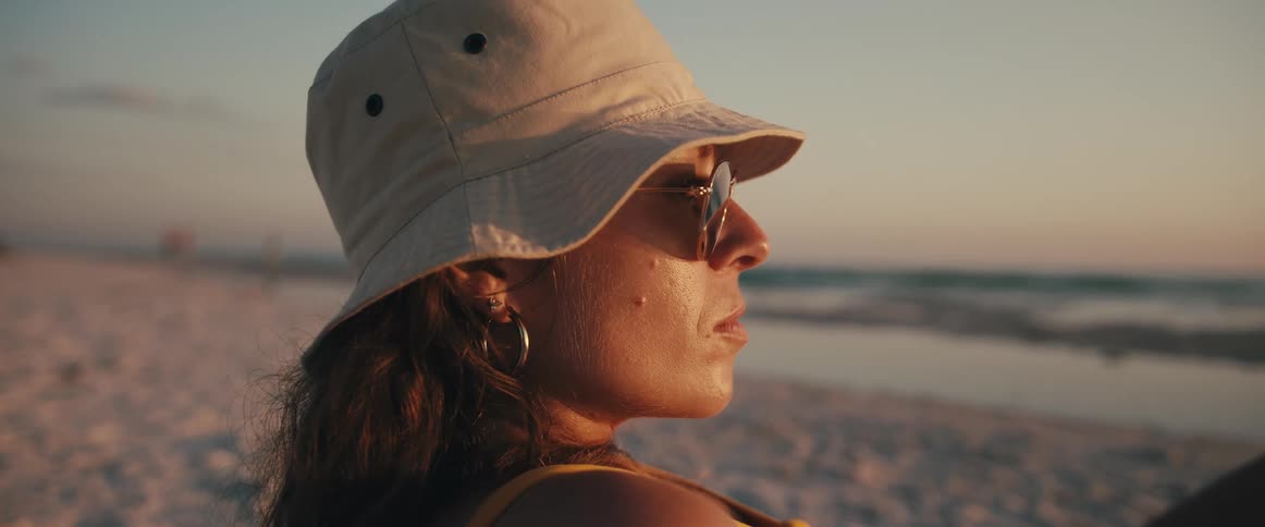 A woman with a hat and sunglasses on a beach with the sky in the background