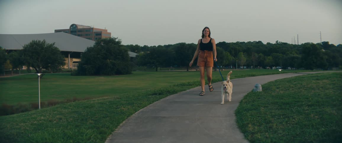 Woman with brown shorts walks a white dog on a track in public park