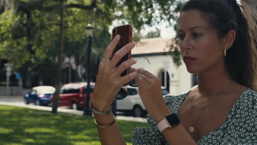 A woman stands outside and holds up her cell phone to see it better