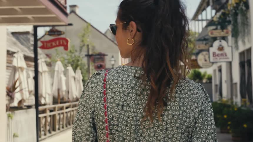 Woman walks along street past shops and an open air cafe