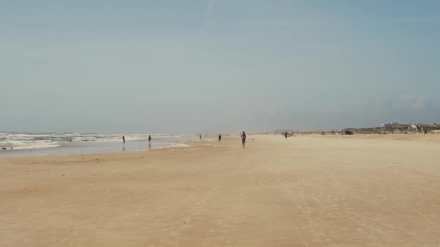 Man in the distance runs towards the camera over the sand on a beach