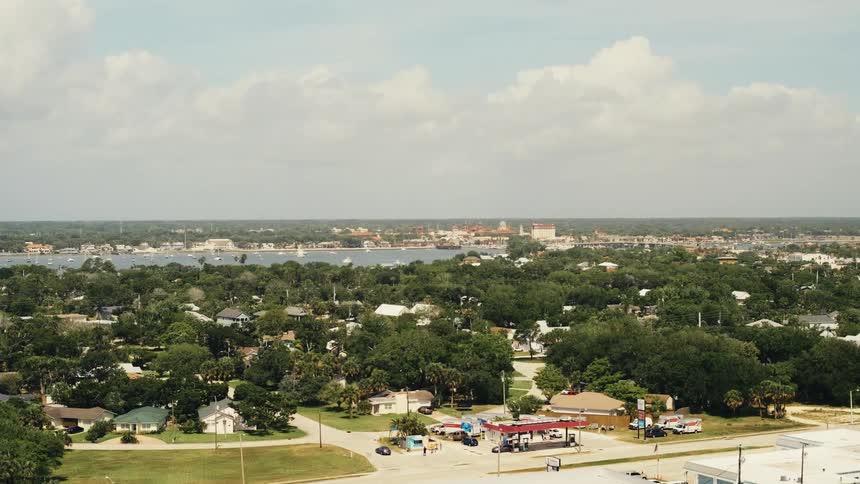 An aerial view of houses and cars driving in a neighborhood with a lake in the distance