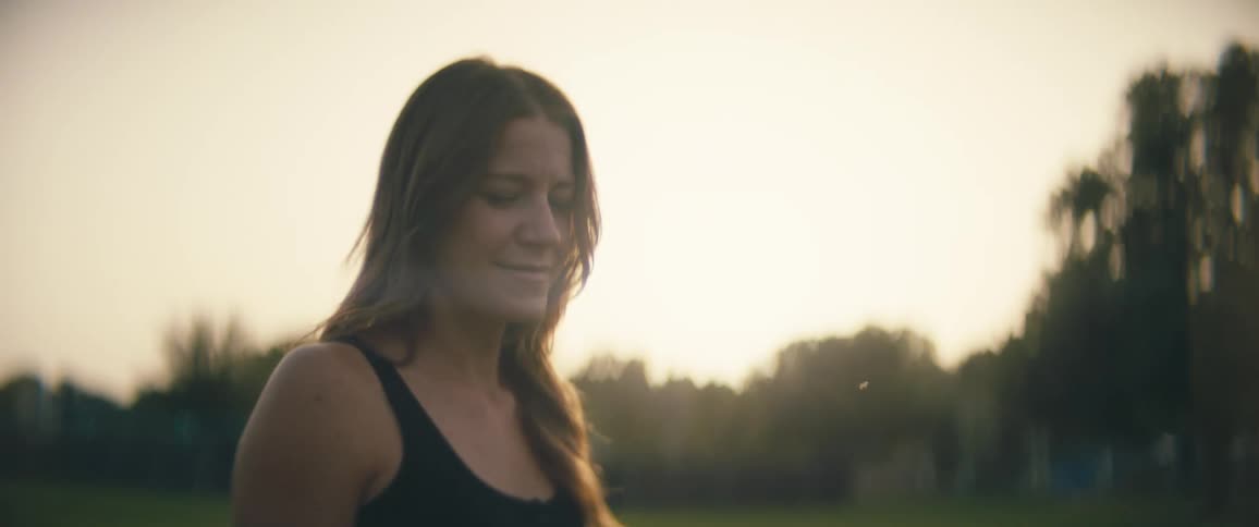 A woman smiles as she walks through a park behind a neighborhood at dusk