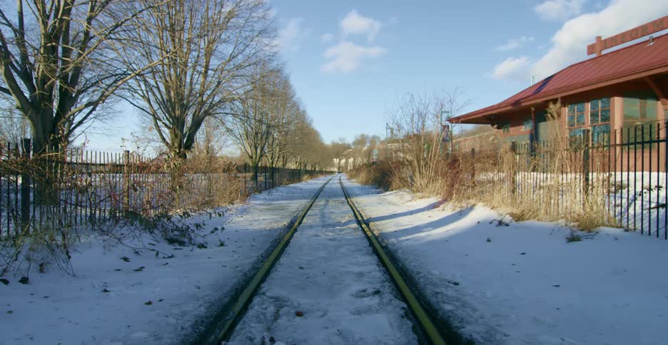 A empty train track beside a red and brown station is covered in snow on a cold winter day