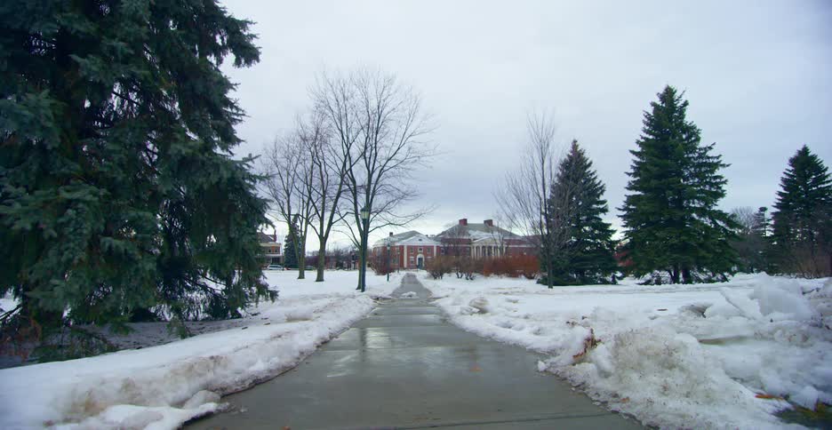 A wet walkway leading to a building through a field covered in snow during the day