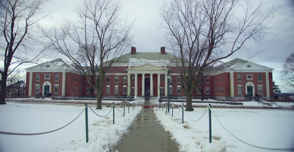 A wet walkway leading through snow towards a large building on a cloudy day