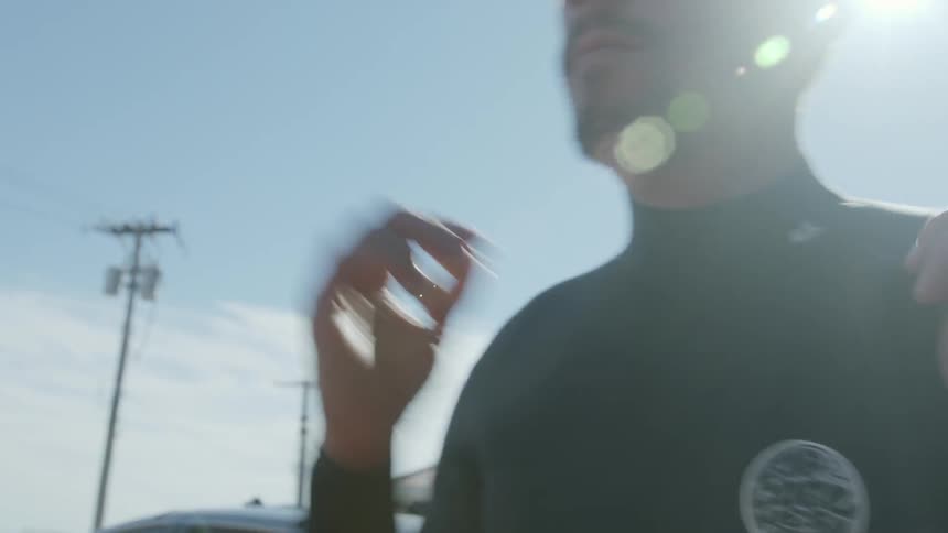A man adjusts his wet suit outside on a sunny day