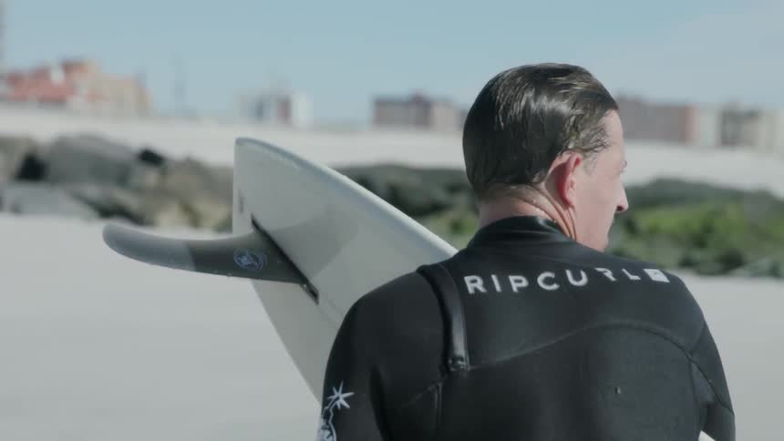 A man in a wet suit carries a surfboard