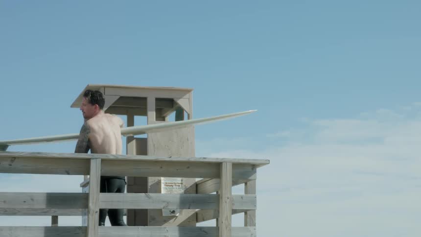A man stands on a balcony holding a surfboard