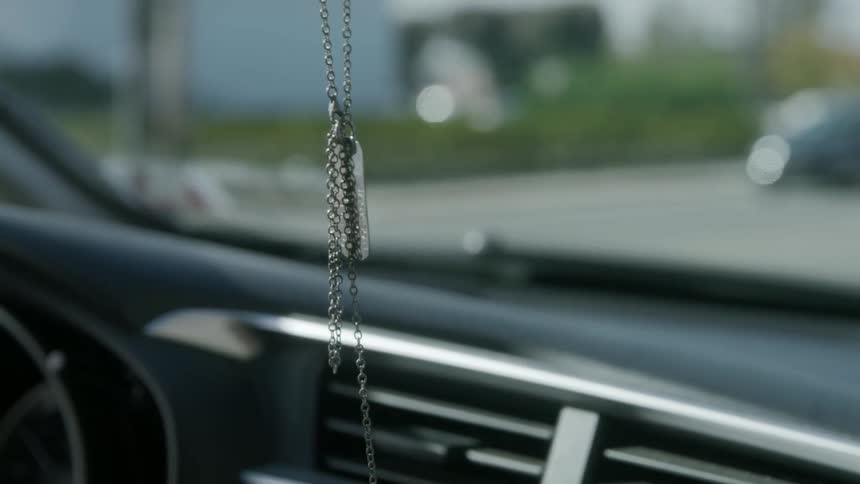 A chain is hanging from the rearview mirror inside a car