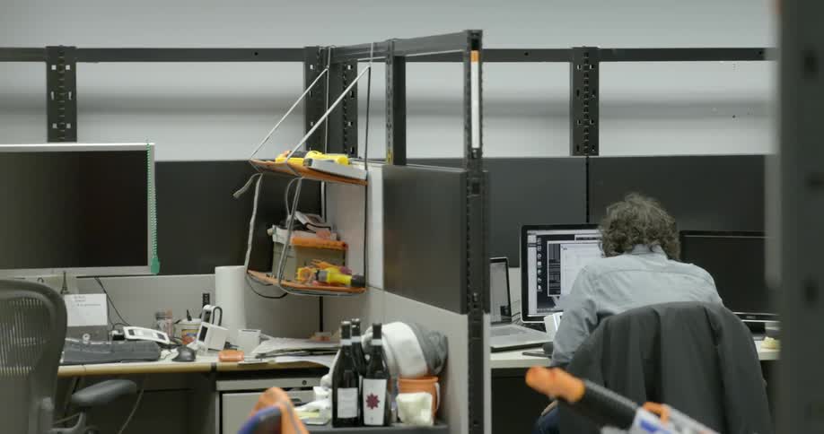 A person with curly gray hair sits at their desk