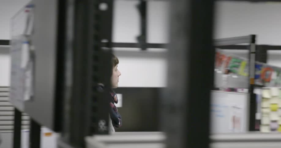 A young woman walks through an office filled with cubicles