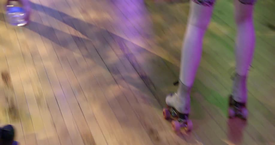 People are skating on a wooden floor with lights flashing