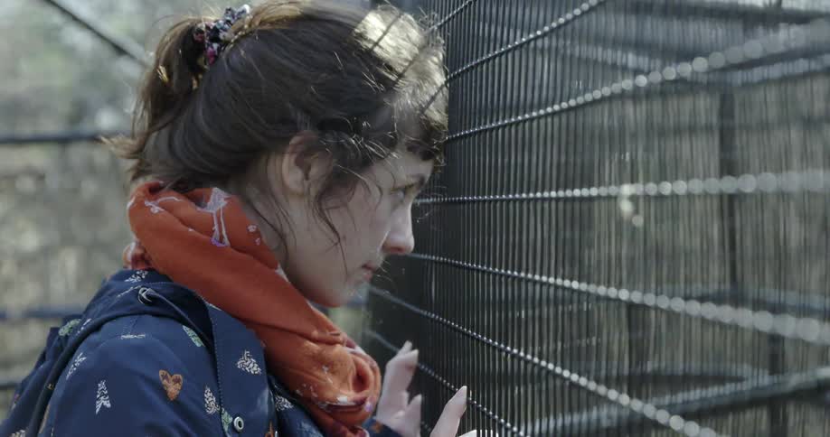 A woman is leaning against a black fence