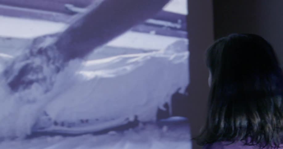 A woman stands and watches a video being projected on a wall
